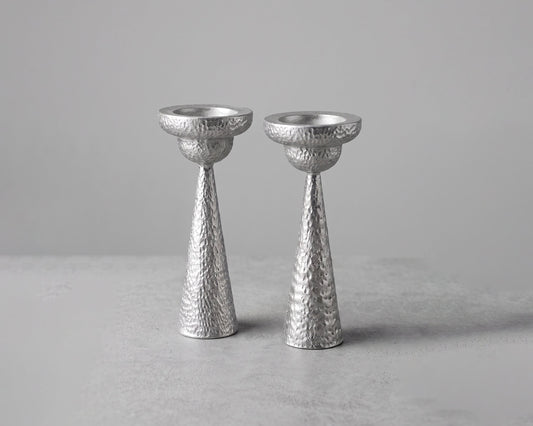 Two textured silver candlesticks standing upright on a light gray surface against a neutral gray background.