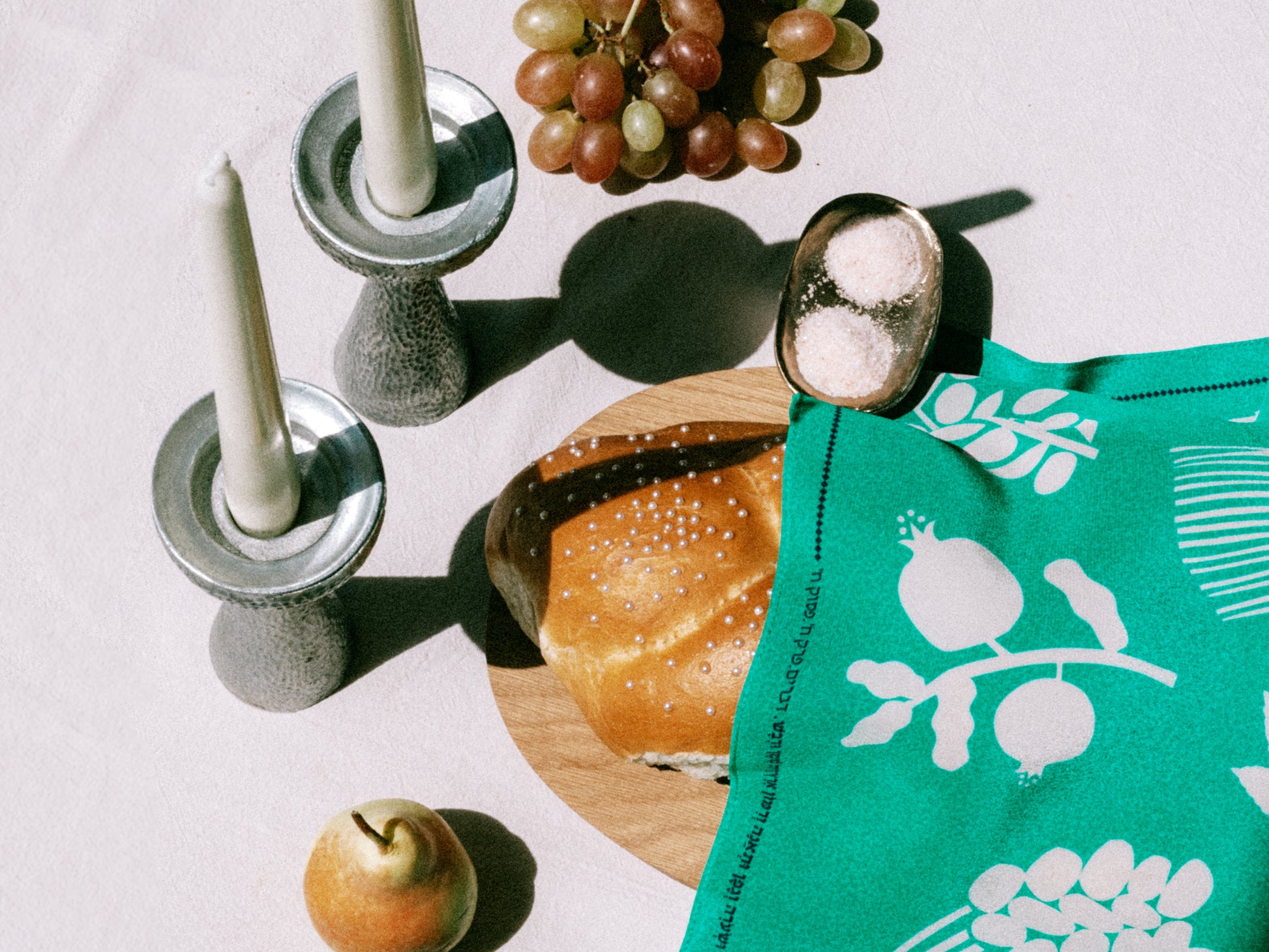 Table setting with bread, grapes, apples, and a green silk challah cover
